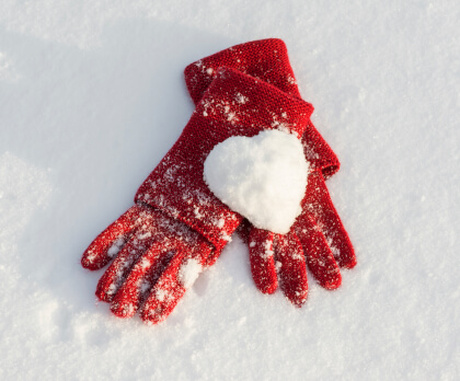Gloves in the snow with a heart shaped snow ball